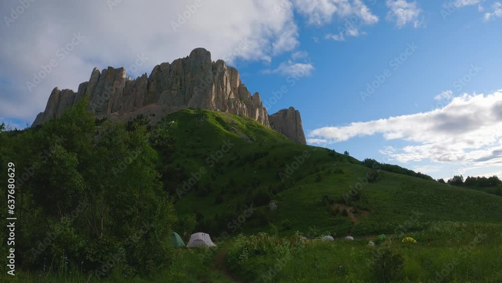 Clouds are passing over the high majestic mountain. Under the city is a tent camp of tourists. Timelapse. Multicoloured tents at the foot of a beautiful mountain Clouds are passing over the high majestic mountain. Under the city is a tent camp of tourists. Timelapse. Multicoloured tents at the foot of a beautiful mountain