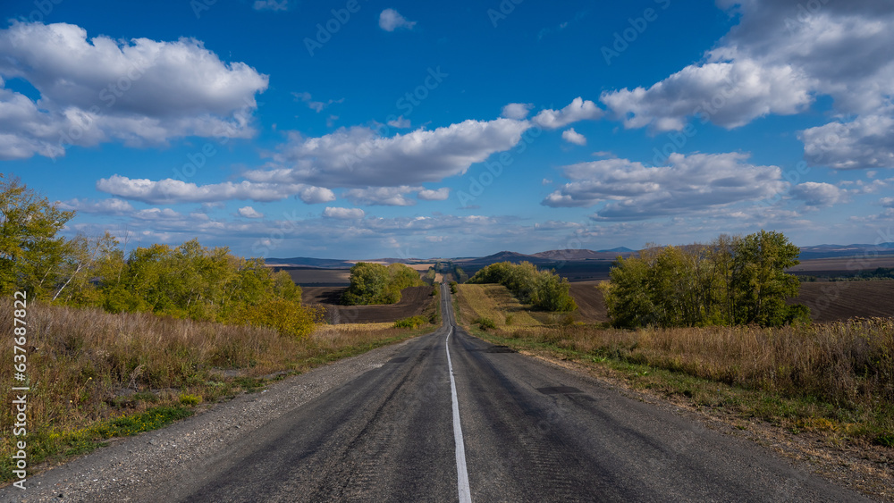 Road landscape. Empty track among mountains and fields in autumn. 