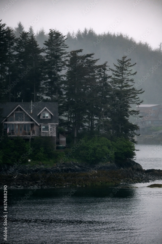 Fototapeta premium Grey, misty, foggy morning in archipelago near Sitka, Alaska with small islands channel cruising and houses