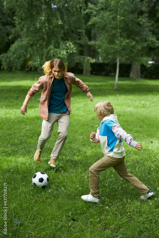 Vertical action shot of father and son playing football together on green grass Vertical action shot of father and son playing football together on green grass