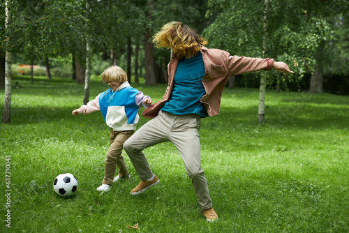 Full length action shot of little boy playing football with father in park, copy space