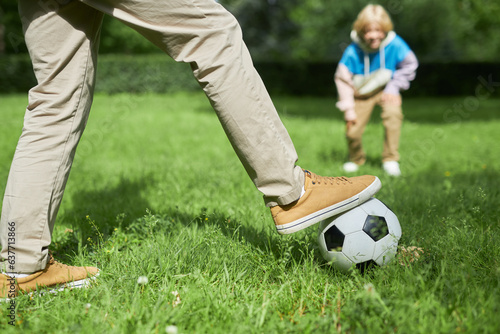 Closeup of adult man playing football with so on green grass in park, copy space