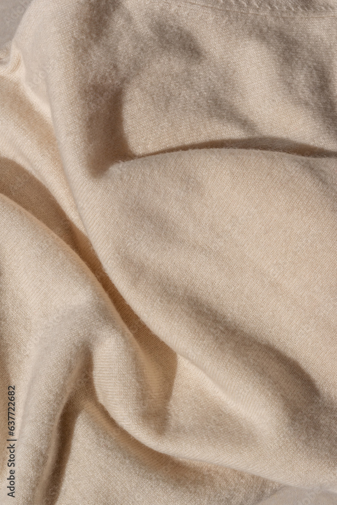 Messy crumpled neutral beige knitwear texture with sunlight and shadow. Soft knitted woolen jersey fabric background.