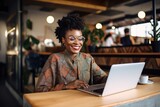 Image of young african american businesswoman in eyeglasses using laptop while sitting in cafe.