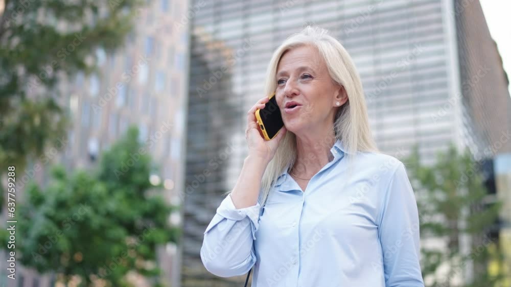 Mature professional woman converses in a lush urban setting with modern structures Mature professional woman converses in a lush urban setting with modern structures