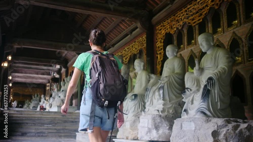 Wallpaper Mural Young female tourist with backpack walking inside traditional vietnamese buddhist temple exploring ancient religious statues and architecture during her travel Torontodigital.ca