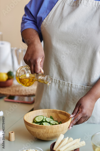 Vertical closeup of black woman adding olive oil to salad while cooking in rustic cozy kitchen