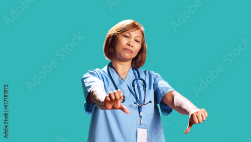 Foto Close up of upset hospital worker showing thumbs down signs while at work, isolated over studio background