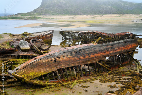 Cemetery of old ships Teriberka Murmansk Russia, wooden remains of industrial fishing boats in sea. Industrialization concept. photo
