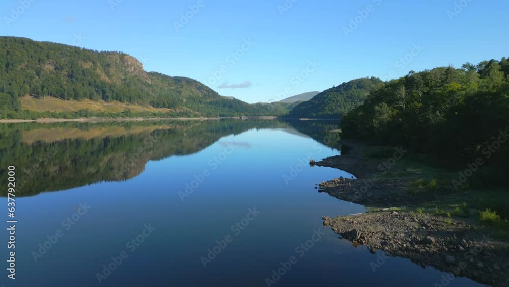 Flying low over calm reservoir with rise revealing woodland and mountains beyond on sunny summer morning at Thirlmere, English Lake District, Cumbria, UK. Flying low over calm reservoir with rise revealing woodland and mountains beyond on sunny summer morning at Thirlmere, English Lake District, Cumbria, UK.