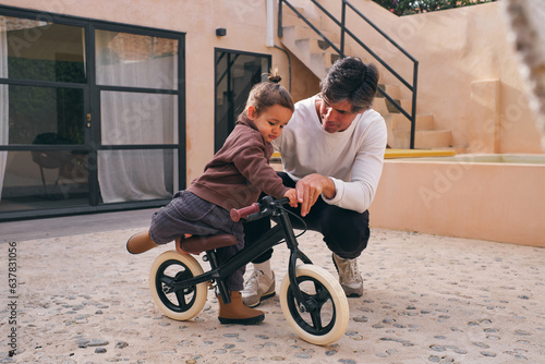 Father interacting with daughter on small bike in patio