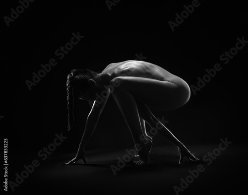 Beautiful sexy fitness girl with a great figure flexing her perfect body in a yoga pose at the studio. Black and white photo