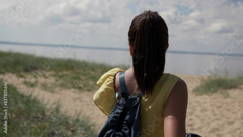 A young brunette girl with long hair looks at the beautiful sun on the beach while holding the handlebars of her bike. The sun is reflected in the sea waves.