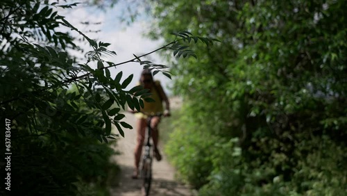 Brunette girl with a backpack rides a bicycle along a path of wooden flooring in a park on the shores of the Gulf of Finland slow motion