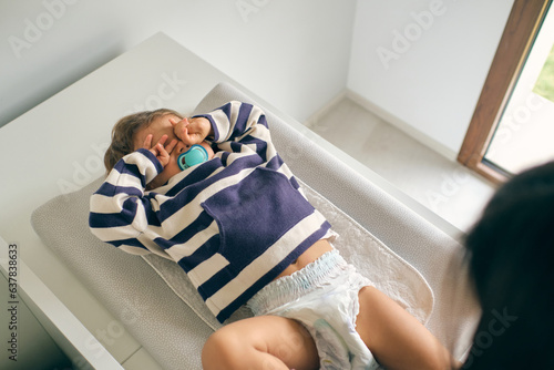 Toddler in nappy lying on changing table and rubbing eyes