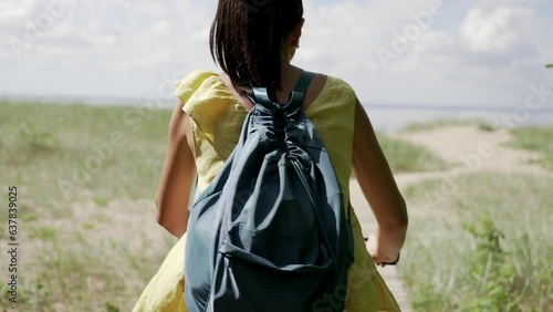 Young brown hair woman with backpack riding bicycle on park, back view. Camera moving forward after her, slow motion effect