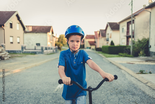Little boy riding scooter. Child playing on suburban street on sunny summer day. Safe helmet for children. Healthy outdoor activity. Cute kid on his way to school.