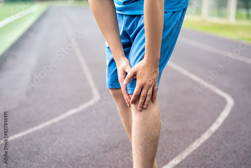 Diseases of the knee joint, bone fracture and inflammation, athletic man on a running track after workout suffering from pain in leg and doing self-massage photo