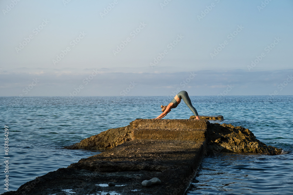 Slim woman doing yoga on pier over sea