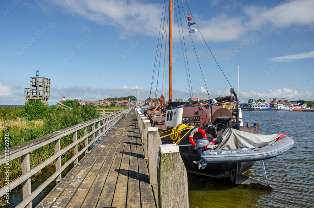 Urk, The Netherlands, August 3, 2023: wooden walkway with moored vessel along the harbour pier with a wooden observation tower