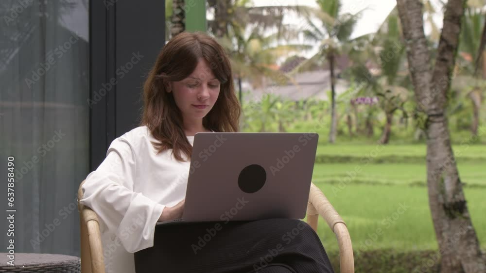 Smiling young business woman typing in laptop computer, tropical palms on the background. Businesswoman working from hotel apartment. Concept of business in internet and traveling Smiling young business woman typing in laptop computer, tropical palms on the background. Businesswoman working from hotel apartment. Concept of business in internet and traveling