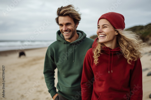 A man and woman wearing red and green hoodies on the beach. AI