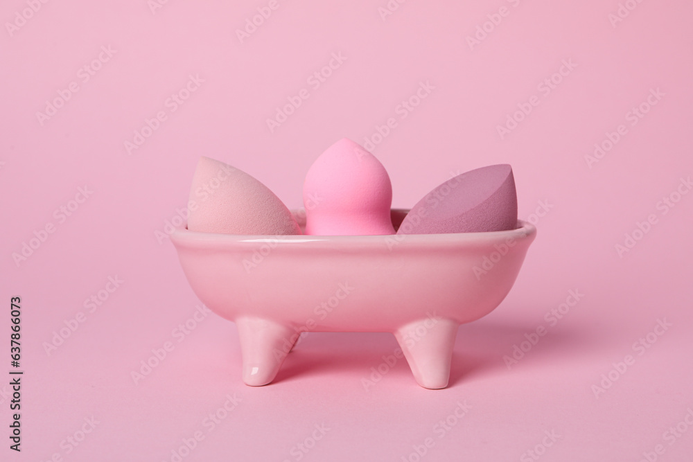 Cosmetic sponges in pink bath on pink background