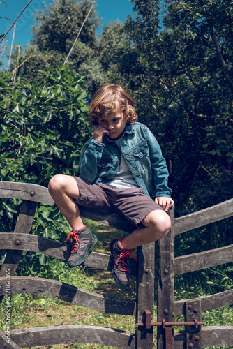 Pensive preteen boy sitting on wooden fence in sunny day