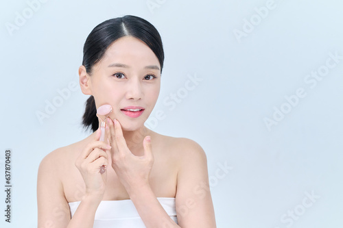 아시아 한국의 검은머리의 젊은 여자 모델이 끈 나시를 입고 핑크색 마사지 롤러를 얼굴에 대고 포즈를 취하고 있다. 