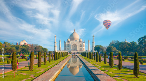 Fotografie Hot air balloon flying over spectacular Taj Mahal, strange clouds in the backgro