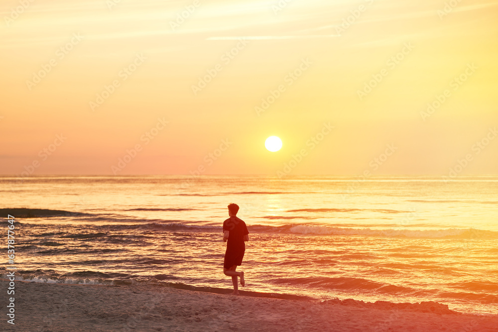 Silhouette of a sportsman running near the ocean shore at sunset.