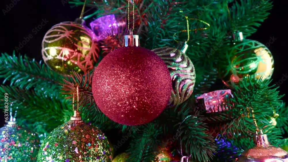 A dark red grainy Christmas ball rotates against a background of Christmas tree branches and garlands decorated with balls A dark red grainy Christmas ball rotates against a background of Christmas tree branches and garlands decorated with balls