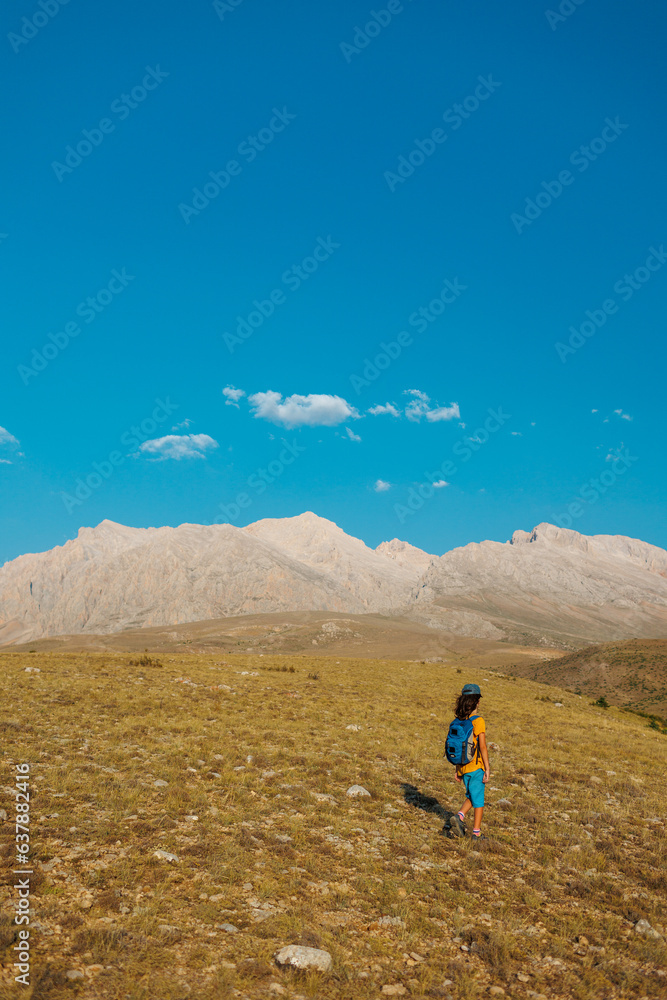 a little boy with a backpack walks along a path against the backdrop of mountains. travel with children to the mountains. Turkey. Aladaglar.