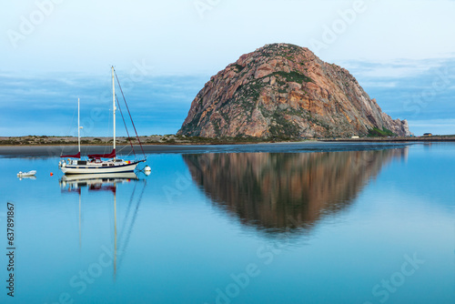 Morning view of Morro Rock in Morro Bay, California. Harbor in foreground with sailboat. Mirror reflection on the water. 
 photo