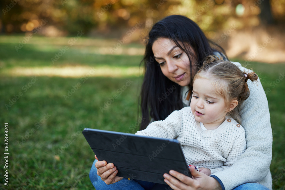 Mother and daughter sitting in autumn park and using digital tablet Mother and daughter sitting in autumn park and using digital tablet