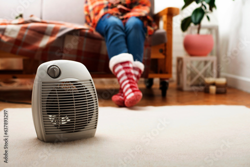 Electric fan heater on the floor in living room with human sitting on the sofa at background