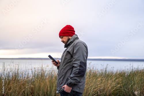 Boy with beard using mobile phone on cloudy day © Gino Gallucci