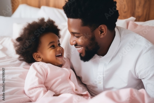 Happy loving young Black dad holding adorable mixed race baby daughter having fun in bed at home. Smiling African father playing with cute funny infant child girl waking up in bedroom in the morning