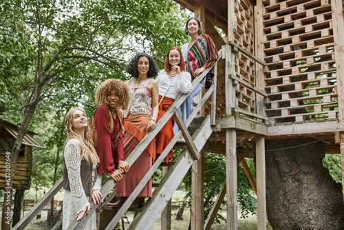 happy multiethnic girlfriends in trendy boho style clothes standing on stairs of retreat center