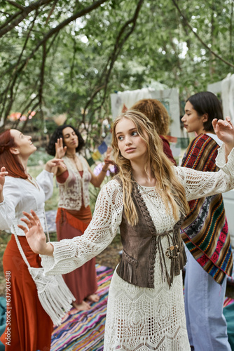 young blonde woman in boho outfit dancing near interracial friends in retreat center