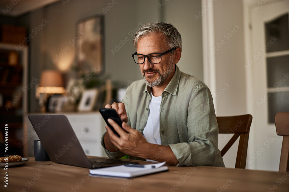 A smiling male freelancer with eyeglasses using a phone while working over a laptop. A smiling male freelancer with eyeglasses using a phone while working over a laptop.
