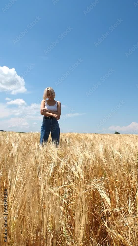 Blonde in white top and jeans stands in a rye field against a clear sky Blonde in white top and jeans stands in a rye field against a clear sky