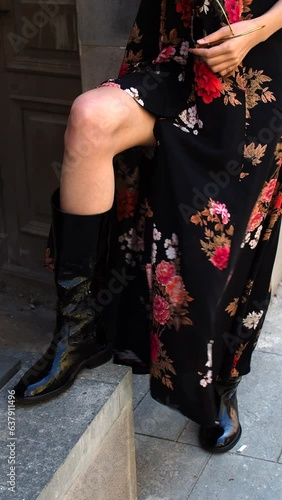 A woman's leg in a leather boot and black floral dress developing from the wind 