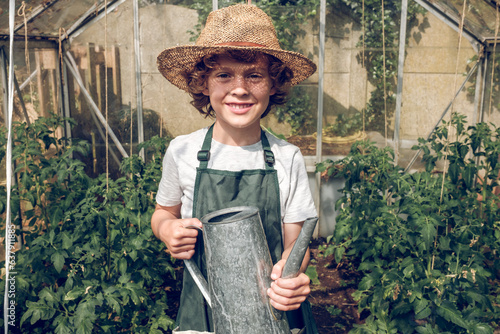 Cheerful preteen boy gardener with watering can in hothouse