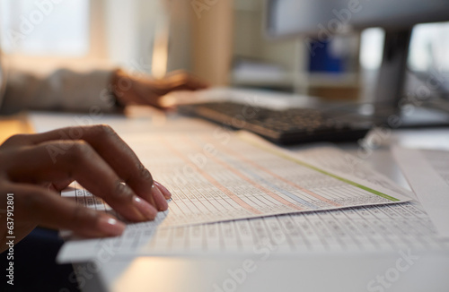 Woman accountant working in the office and doing business paperwork. Close up of the hand of an African American woman on a paper data sheet, with a computer in the background