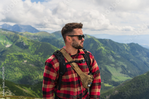 Portrait of a man with a beard in sunglasses and a shirt, a traveler in the Tatra mountains in summer.