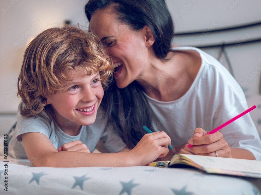 Cheerful boy and happy mother painting together lying on bed Cheerful boy and happy mother painting together lying on bed
