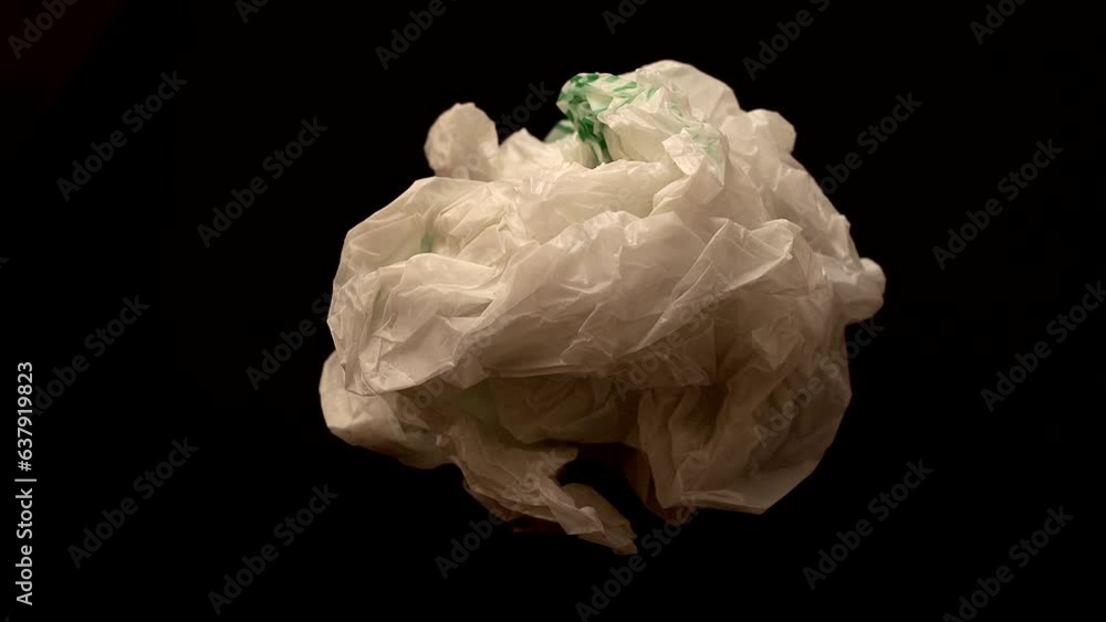 A crumpled white plastic bag straightens out on a black background A crumpled white plastic bag straightens out on a black background