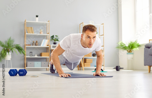 Portrait of a young attractive sporty man doing push-up or plank sport exercises lying on yoga mat on the floor in the living room at home. Fitness, workout and home training concept. photo