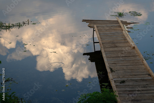 light wooden bridge. Fishing platform. Reflection of clouds in the river. Bridge to the clouds. Fishing. Summer evening on the river.